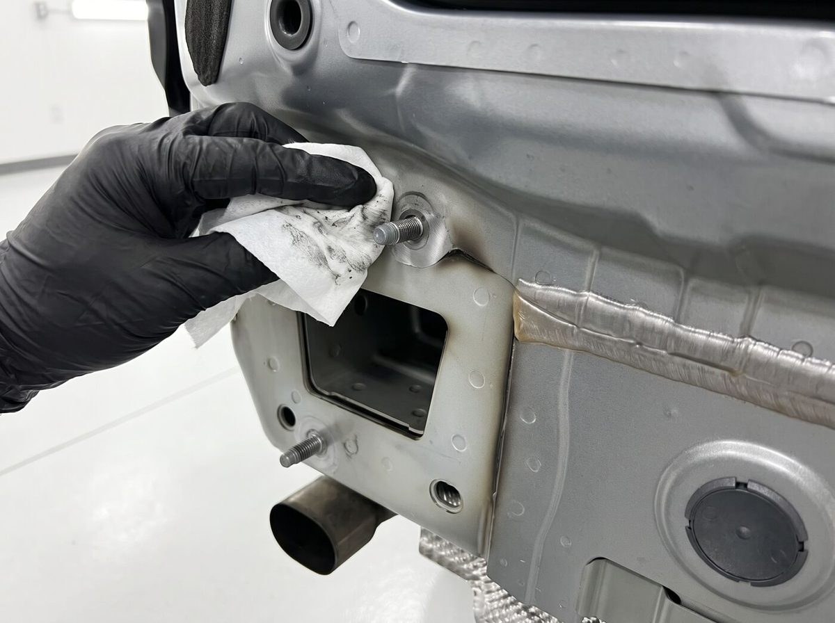 Technicien en gants nettoyant un point d'ancrage sur le châssis d'un véhicule en atelier