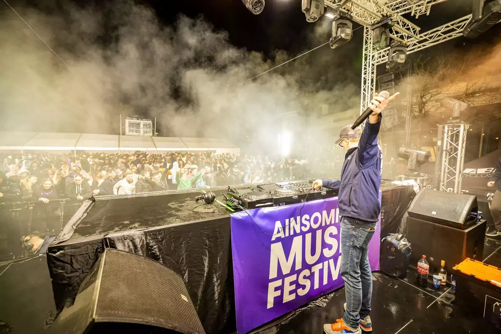 DJ en casquette lève le micro vers une foule nombreuse sur scène extérieure